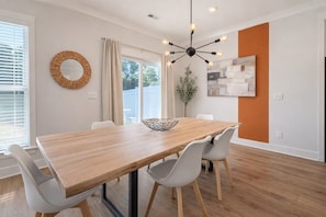 A dining area with a wooden table, white chairs, a woven mirror, and a modern light fixture.