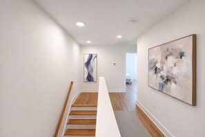 Un intérieur moderne avec un escalier, un plancher en bois et des œuvres d’art abstraites accrochées au mur.