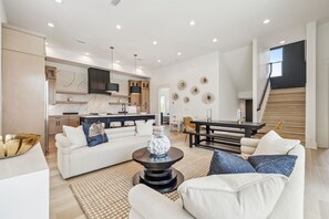 A spacious living area with a sofa, coffee table, and dining table. A kitchen is visible in the background with modern appliances and cabinetry. - Brand New! 30A! Private Pool. Free Bikes. (Santa Rosa Beach)