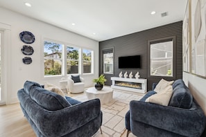 A modern living room with a fireplace, a flat-screen TV, and a large window. - Brand New! 30A! Private Pool. Free Bikes. (Santa Rosa Beach)