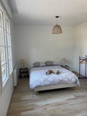 Un dormitorio con cama, dos mesitas de noche, lámpara colgante, radiador y ventana.