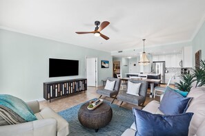 A modern living room with a flat-screen TV, a ceiling fan, and a dining area with a kitchen in the background. - Topsl Summit Condo! Pools/Beach. Ocean View! (Miramar Beach)