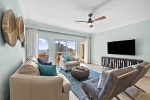 Un salon comprenant un canapé, un fauteuil, un pouf et un ventilateur de plafond.