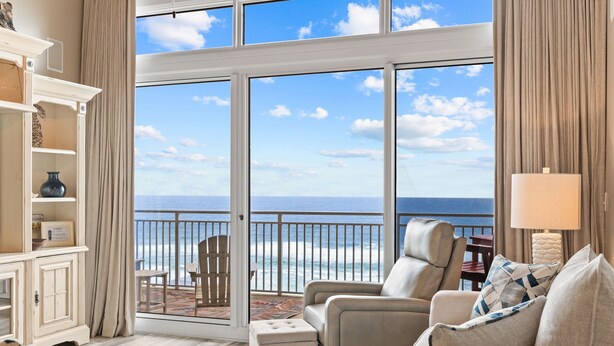 A spacious living room with a large sliding glass door leading to a balcony with a view of the ocean. - Private Beach! Chair setup! Penthouse. Destin! (Destin)