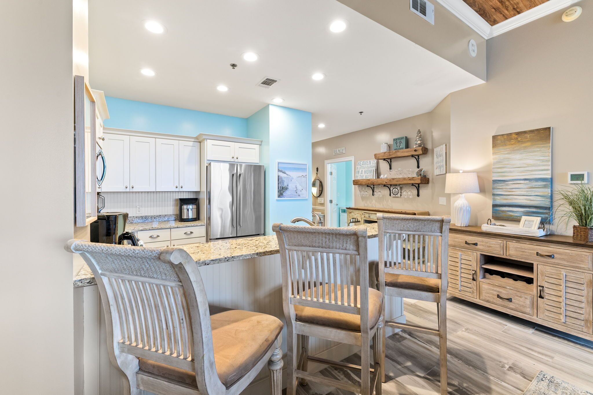 A modern kitchen with white cabinets, a granite countertop, and a dining area with wooden chairs.