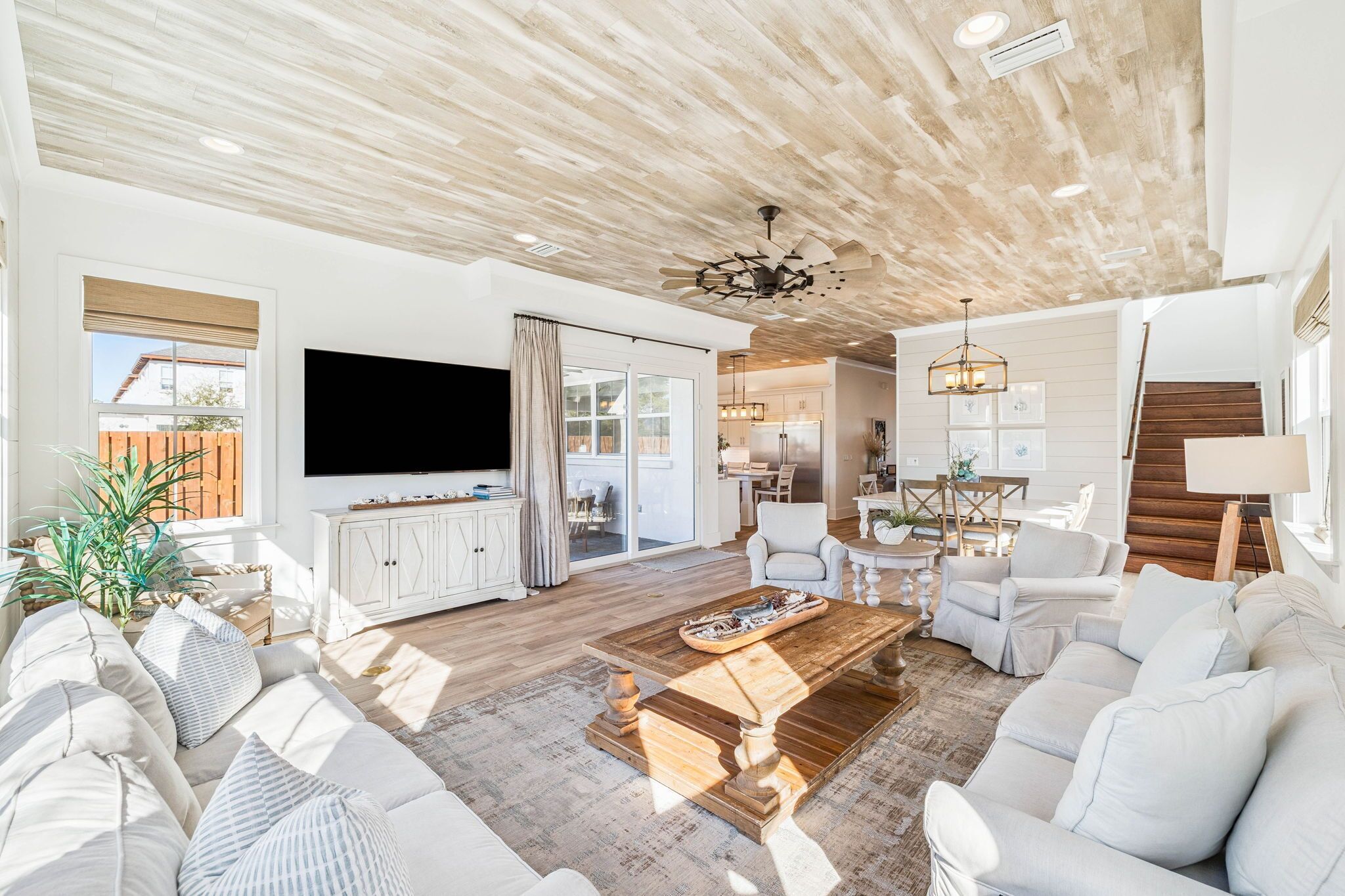 A spacious living room with a large flat-screen TV, a wooden ceiling, and a dining area with a chandelier.
