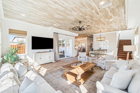 Ein geräumiges Wohnzimmer mit einem großen Flachbildfernseher, einer Holzbalkendecke und einem Essbereich mit einem Chandelier.