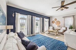 Ein Wohnzimmer mit blauem Teppich, weißen Sofas und einem Deckenventilator.