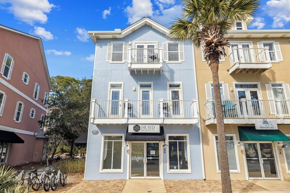 A multi-story building with balconies, a sign for Hurd Real Estate & Co., and a green awning. - Updated! Beach Access - Pool - Walkable Dining (Santa Rosa Beach)