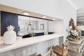 Eine moderne Küche mit weißem Arbeitsplatz, dunklen Schränken und einem Holztisch.