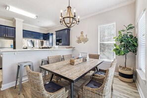 A modern kitchen with dark blue cabinets, a central island, and a dining area with wicker chairs and a wooden table. - Updated! Beach Access - Pool - Walkable Dining (Santa Rosa Beach)