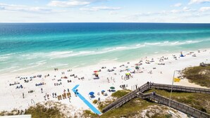 A beach with a wooden boardwalk leading to the water, a sandy beach, and a clear blue sky.