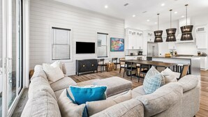 A modern living room with a sofa set, a dining area, and a kitchen with white cabinetry.