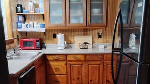 Une cuisine avec des meubles de rangement en bois, un réfrigérateur, un four à micro-ondes et une machine à café.