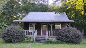 Une maison en bois à l’allure rustique, dotée d’un porche, d’une porte d’entrée et d’un petit jardin devant.