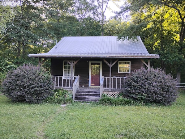 A rustic wooden house with a porch, a front door, and a small front yard.
