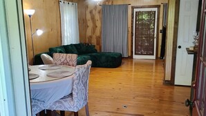 Une pièce spacieuse avec un plancher en bois, une table à manger entourée de chaises, un canapé vert et un ventilateur de plafond.