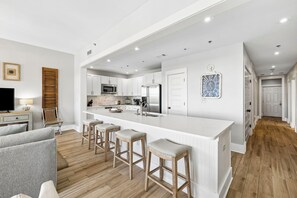 Eine moderne Küche mit weißen Schränken, einer großen Kochinsel mit Sitzgelegenheiten und einem Essbereich mit grauem Sofa.