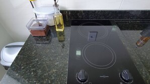 A kitchen with a black induction cooktop, a white countertop, a bottle of oil, and a container of food. - Family apartment, calm and welcoming, with beach and park nearby. (Penha SC)