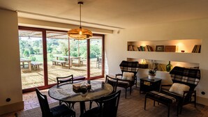 A dining area with a round table, chairs, a hanging light fixture, and a view of the outdoors through large glass doors. - Casa Villae Relais & Châteaux - The most charming house in the Dão region (Silvã de Cima)
