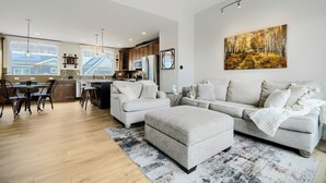 Uma sala de estar moderna com sofá, banquinho e área de jantar com cadeiras e mesa.