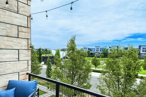 A balcony with a stone wall, a blue chair, and a view of modern buildings and greenery. - Central Park Townhome | 30-Day+ | Pets & Garage, Utilities included (Denver)