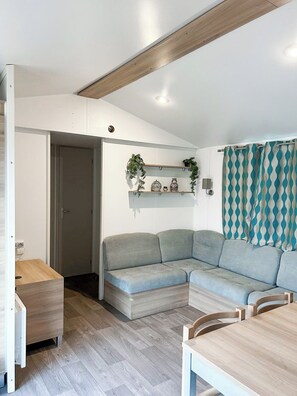 A modern living room with a sectional sofa, a wooden dining table, and a built-in shelf with decorative items. - Unit 25 Les Amandiers - Spacious, bright and ideal for families (Lévignac-de-Guyenne)