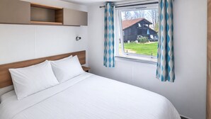 Un dormitorio con una cama, cabecera de madera, ventana con cortinas y un estante pequeño sobre la cama.