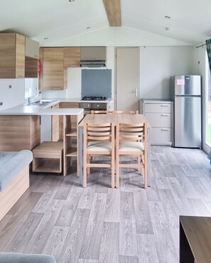 A modern kitchen with a dining area, wooden cabinets, and a built-in stove. - Unit 25 Les Amandiers - Spacious, bright and ideal for families (Lévignac-de-Guyenne)