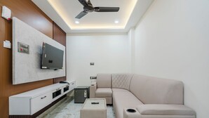 A modern living room with a flat-screen TV, a sofa, a coffee table, a ceiling fan, and a small safe. - Hotel Rasaballa grand (Kothagudem)