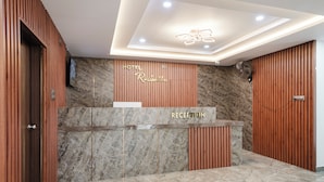 A hotel reception desk with a marble countertop, wooden paneling, and a ceiling with recessed lighting. - Hotel Rasaballa grand (Kothagudem)