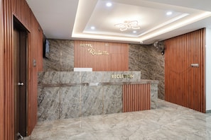 Un mostrador de recepción de hotel con encimera de mármol, paneles de madera e iluminación empotrada en el techo.
