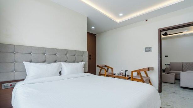 A hotel room with a large bed, a wooden side table, a chair, a sofa, and a mirror. - Hotel Rasaballa grand (Kothagudem)