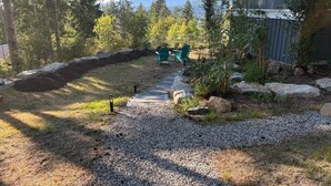 Ein Garten mit Kiesweg, zwei grünen Stühlen, einer Holzterrasse und einer Steinmauer.