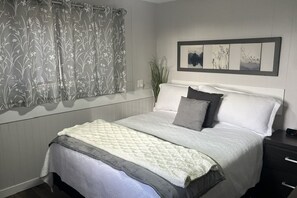 Un lit bien fait, avec une couverture, des oreillers et une table de chevet sur laquelle se trouve une lampe.