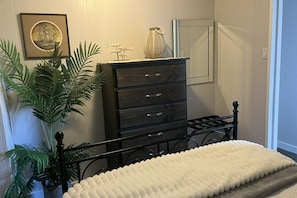 Un dormitorio con cama, cómoda, planta en maceta y un cuadro en la pared.
