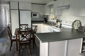 A modern kitchen with white cabinetry, a central island, a microwave, a coffee maker, and a stove.