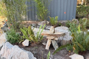 Un jardín con una estructura de piedra, bambú, helechos y una cerca de madera.