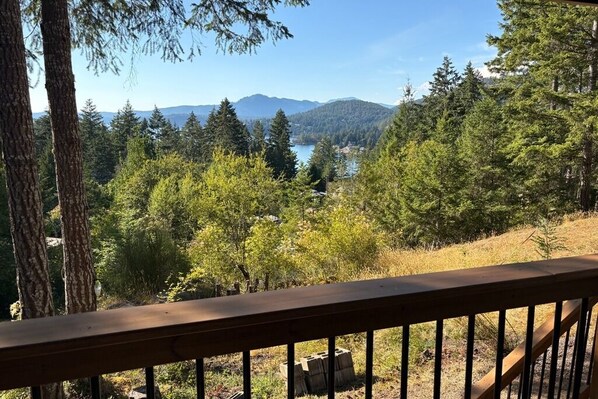 A view from a wooden deck overlooking a forested area with a lake and mountains in the distance.
