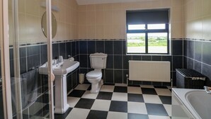 A bathroom with a checkered floor, a toilet, a sink, a window, and a radiator. - Strand House (Bannow)