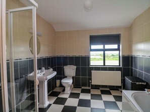 A bathroom with a checkered floor, a toilet, a sink, a window, and a radiator. - Strand House (Bannow)