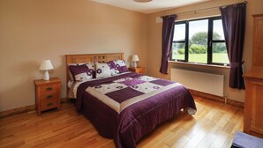 A bedroom with a wooden bed, two bedside tables, a window with curtains, and a radiator. - Strand House (Bannow)