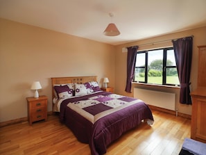 A bedroom with a wooden bed, two bedside tables, a window with curtains, and a radiator. - Strand House (Bannow)