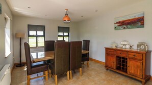 A dining area with a table and chairs, a pendant light, a radiator, a cabinet with drawers, and a painting on the wall. - Strand House (Bannow)