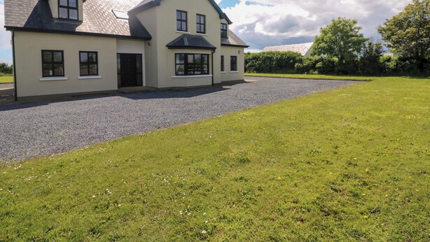 A two-story house with a gravel driveway and a grassy lawn. - Strand House (Bannow)