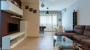 Ein Wohnzimmer mit Fernseher, Sofa, Glastisch und einem Essbereich mit Stühlen und Tisch.
