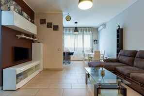 Ein Wohnzimmer mit Fernseher, Sofa, Glastisch und einem Essbereich mit Stühlen und Tisch.