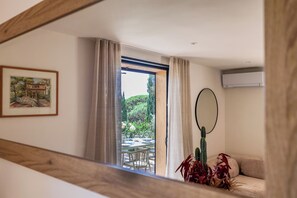 A room with a view of an outdoor dining area, a framed picture on the wall, a cactus plant, and a ceiling-mounted air conditioning unit.