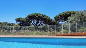 Une piscine, avec un ciel bleu dégagé, des arbres et une clôture.