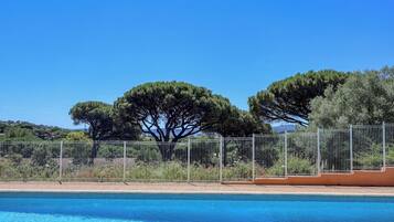 Une piscine, avec un ciel bleu dégagé, des arbres et une clôture.
